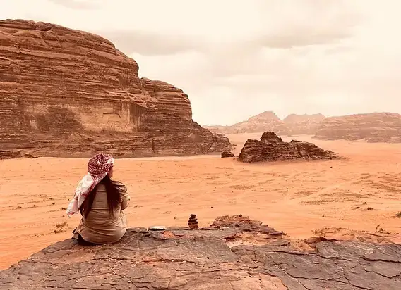 Traveler sitting on the soft desert sand facing rocky cliffs in Wadi Rum