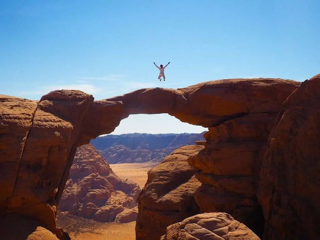 Man jumping on a natural rock bridge during a Wadi Rum jeep tour adventure