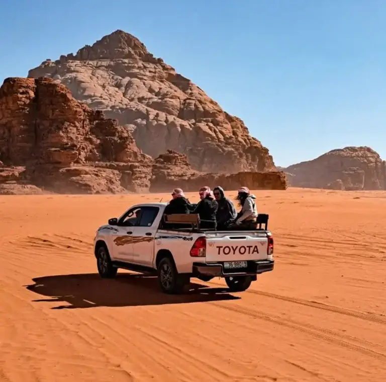 4x4 jeep driving across the red sand dunes of Wadi Rum with desert mountains in the background