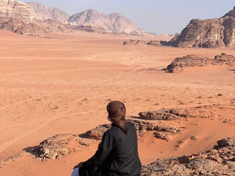 Solo traveler sitting on a rock and admiring the vast desert landscape of Wadi Rum